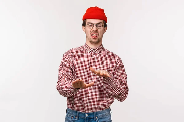 Portrait drôle jeune homme réticent en bonnet rouge et des lunettes, serrant la main dans le rejet, bâton de langue et grimaçant dégoûté, exprimer sa désapprobation et détester ou chose horrible laid, fond blanc — Photo