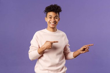 Korkulu genç Avrupalı bir gencin portresi, hippi erkek öğrenci çevrimiçi kurslara katılıyor, süper havalı abonelik ücretini ödüyor, parmaklarını sağa gösteriyor, kameraya gülümsüyor,