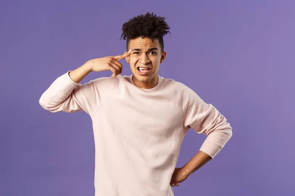 Portrait of angry, annoyed young man scolding someone from being stupid and crazy, rolling index finger over temple staring outraged and irritated camera, standing bothered purple background — Stock Photo, Image