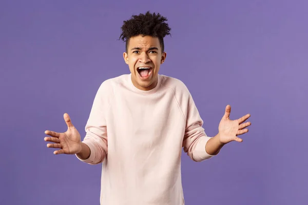 Portrait of concerned, upset and frustrated young man cant believe he lost, asking why, spread hands sideways in dismay, complaining shouting angry and uneasy, standing purple background — Stock Photo, Image