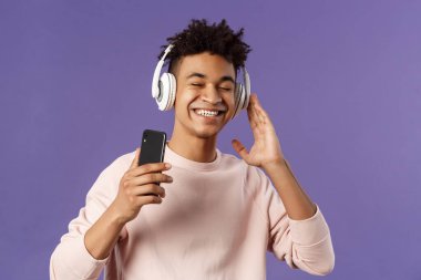 Teknoloji ve yaşam tarzı konsepti. Kaygısız, çekici genç bir adamın portresi. Sesin tadını çıkarıyor, kulaklıkla müzik dinliyor. Harika bir bas kalitesi, cep telefonu var.
