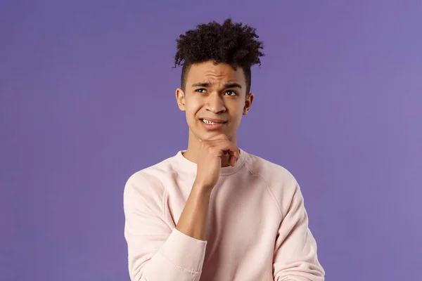 Close-up portrait of indecisive, puzzled young man facing difficult choice, look up thoughtful, touch chin and grimacing while thinking, making-up idea or decision, purple background — Stock Photo, Image