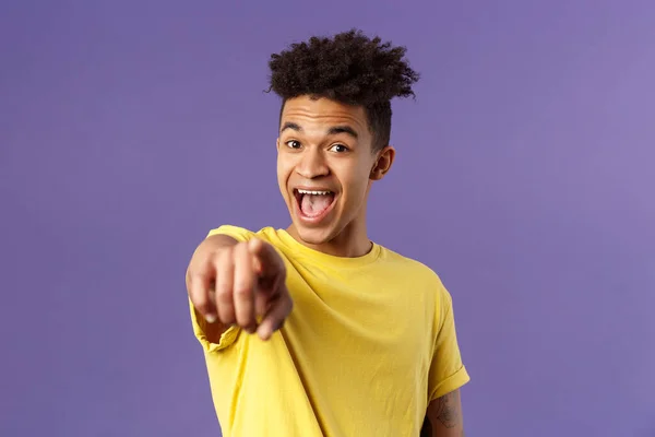 Retrato de primer plano del optimista y sorprendido hombre hispano con rastas, joven estudiante señalando con el dedo a la cámara y riendo, reconocer a alguien familiar, de pie fondo púrpura —  Fotos de Stock