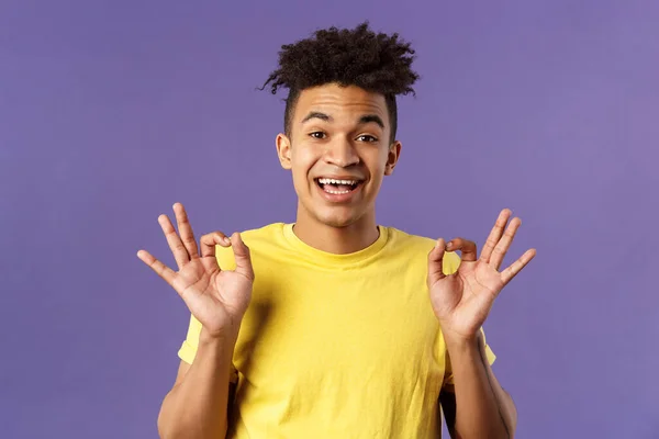 Primer plano retrato de optimista, relajado joven hipster chico con rastas asegurando todo lo bueno, todo estará bien, mostrar gesto OK y sonriendo, sin problema garantía de la mejor calidad, fondo púrpura —  Fotos de Stock