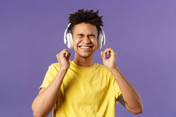 Retrato del joven contento y emocionado disfrutando de ritmos impresionantes de buena calidad en auriculares, ojos cerrados y regocijo sonriente, bailando sobre una nueva canción genial, escuchar música sobre fondo púrpura —  Fotos de Stock