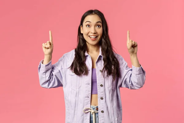 Entusiástico jovem bonita menina olhando e apontando os dedos para cima com sorriso feliz, ver promo, interessado em participar do evento, festa, encontrou grandes cursos on-line, de pé fundo rosa — Fotografia de Stock