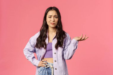 Ne olmuş, umurumda değil. Şüpheci, etkilenmemiş, dikkatsiz, stil düşkünü kızın portresi, omuz silkip korkuyla el kaldırın, saçmalıkları dinleyin, pembe arka plan