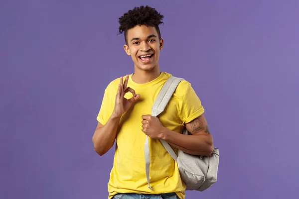 Zurück zur Schule, zum Universitätskonzept. Porträt des jungen hübschen Hipster-Typen, Student mit Rucksack versichern Test gut sein, zeigen okay Zeichen, chillen und entspannen keine Sorgen, alles ok, lila Hintergrund — Stockfoto