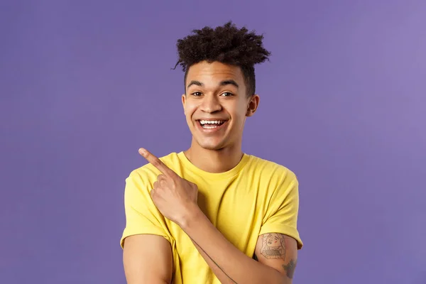 Close-up portrait of cheerful, attractive young male student showing promo, pointing at upper left corner, smiling pleased, recommend click link, visit page or download app, purple background — Stock Photo, Image