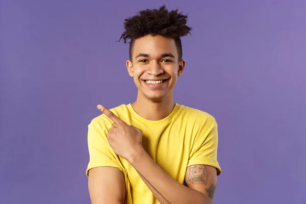 Close-up portrait of enthusiastic, happy young hipster male with dreads, beaming smile and pointing finger upper left corner, present cool product, introduce something really good, purple background — Stock Photo, Image