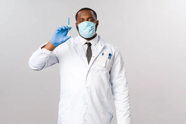 Covid-19, traitement du coronavirus et concept de laboratoire. Médecin afro-américain professionnel sérieux prêt à guérir, seringue avec vaccin bleu, masque facial et gants en latex — Photo