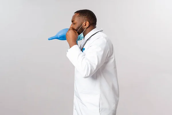 Covid-19, coronavirus 환자 치료 및 질병 개념. 웃기게도 젊은 아프리카 계 미국인 남자 의사 가 직장에서 휴식을 갖고 라텍스 장갑에 공기를 불어넣으며 — 스톡 사진