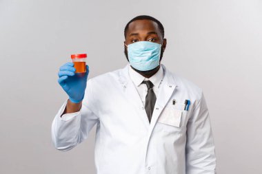 Covid19, pandemic and healthcare concept. African-american doctor in face-mask and latex gloves, study medical tests, got urinalysis from patient showing it, standing grey background clipart