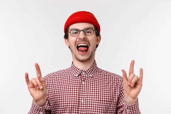 Close-up retrato engraçado bonito barbudo jovem adulto cara em gorro vermelho, óculos grito otimista e animado, mostrando rock-n-roll, gesto de heavy metal desfrutando de festa incrível, de pé fundo branco — Fotografia de Stock