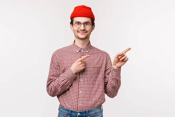 Midja upp porträtt av nöjd glad glad leende ung hipster kille i röd mössa, glasögon pekar finger rätt topp annons med nöjda uttryck, fann utmärkt produkt eller företagstjänst — Stockfoto