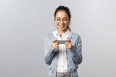 Teknoloji, online ve mobil yaşam tarzı konsepti. Neşeli genç hevesli Asyalı kız telefonu kullanıyor, yeni oyunu oynamak için akıllı telefonu yatay olarak tutuyor, yarış uygulaması ya da atari salonu yüklüyor.