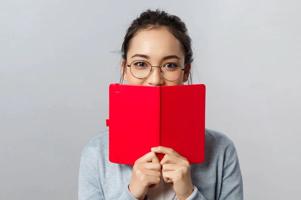 Bildung, Universität und Volkskonzept. Nahaufnahme Porträt einer romantischen jungen Studentin, asiatische Mädchen haben geheimes Tagebuch, versteckt Lächeln hinter Planer oder Notizbuch, Notizen schreiben, grauer Hintergrund — Stockfoto