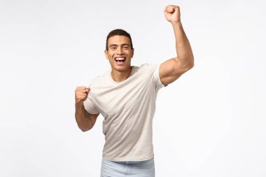 Adam el kaldırıyor ve favori spor takımı için tezahürat yapıyor. Yakışıklı, genç, güçlü bir adam yumruk tokuşturuyor ve gülümsüyor, arkadaşını cesaretlendiriyor, birini destekliyor, beyaz arka plan üzerine bahse giriyor.