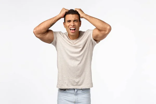 Homem atlético decepcionado em t-shirt, pegue a cabeça e puxe o cabelo incomodado, franzindo a testa chocado e frustrado, perdeu muito dinheiro, se sentir traído ou decepcionado, de pé fundo branco angustiado — Fotografia de Stock