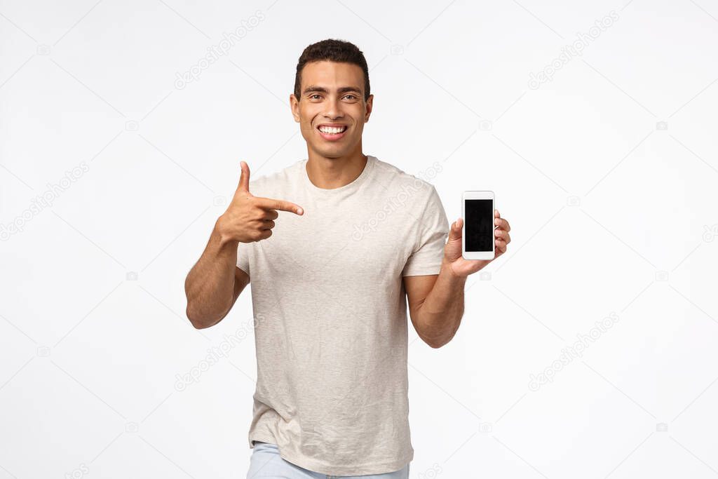 Technology, mobile gadget and people concept. Cheerful good-looking brazilian athletic man recommend fitness app, looking at calories or diet advices, holding smartphone, pointing mobile, smiling