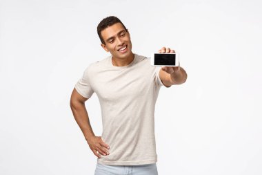 Etkileyici, yakışıklı İspanyol görünümlü, iyi görünümlü, fitness uygulamasını destekleyen, gülümseyen, elini uzatan, akıllı telefon tutan, reklam uygulaması, beyaz arka plan