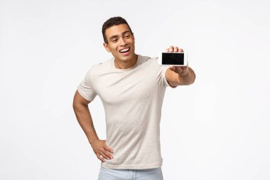 Adam yeni mobil oyun oynamayı seviyor, tavsiye indirme uygulaması. Şaşırmış bir şekilde gülümseyen, mutlu ve güçlü genç adam, akıllı telefonu yatay olarak tutuyor, neşeli bir sırıtışla cihaz ekranına bakıyor.