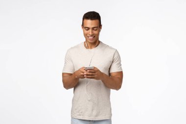 İletişim, teknoloji ve mobil cihaz konsepti. Sıradan kıyafetler içindeki yakışıklı atletik adam, kulaklık takan, akıllı telefonu tutan ve gülümseyen cep telefonu görünümlü ekran, mesaj arkadaşı, metroda video izleyen.