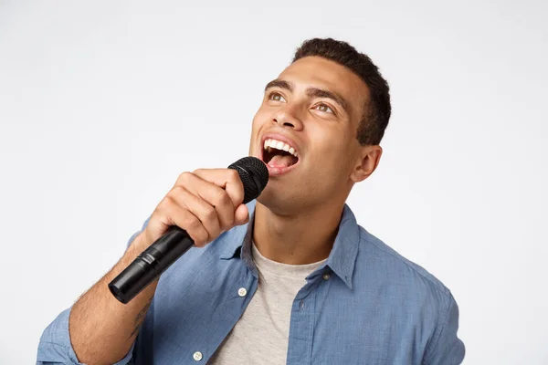 Carefree good-looking young man having fun during christmas party, singing favorite song, hold microphone bending as reading lyrics on screen, enjoy spend time karaoke bar, stand white background
