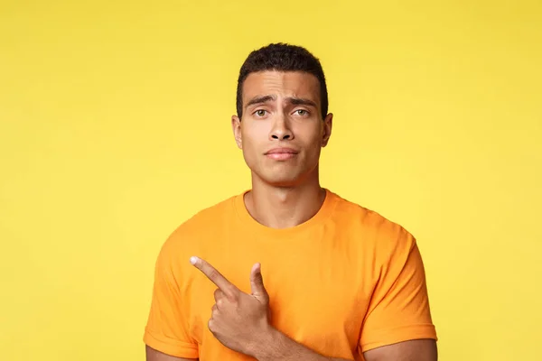 Upset and depressed young handsome sportsman in casual outfit, frowning making gloomy frustrated expression, regret missed chance, pointing upper left corner, feel lonely or uneasy, yellow background — Stock Photo, Image