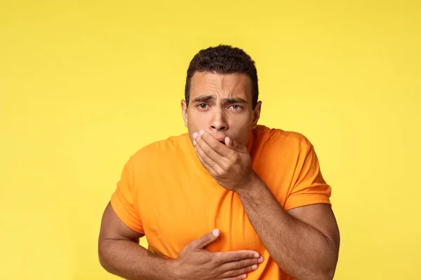Masculine man want vomit, feeling sick and unwell, ate too much junk unhealthy food, touching stomach and cover mouth with palm as standing yellow background sick, puke from disgust — ストック写真