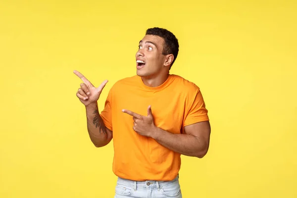 Surpris, excité beau mec sans voix en t-shirt orange, haletant fasciné, regard et pointant coin supérieur gauche à la promotion fantastique, voir mot de passe magnifique pendant le compte à rebours du nouvel an — Photo