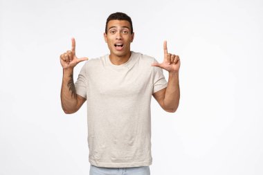 Şaşırmış ve heyecanlı İspanyol tişörtlü yakışıklı kaslı erkek, parmaklarını havaya kaldırıp kameraya bakıyor, etkilenmiş, ağzı açık, nefes nefese kalmış, yeni ürüne bakın.