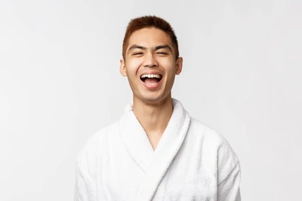 Beauty, Wellness- und Freizeitkonzept. Fröhlicher asiatischer Mann, der die Wochenenden verbringt, um sich an heißen Quellen zu entspannen, Bademantel lachend trägt, Urlaub genießt, sich im Hotelresort erholt, weißer Hintergrund steht — Stockfoto
