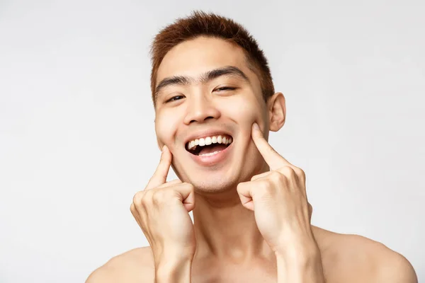 Szépség, bőr és férfi egészség koncepció. Fejlövés boldog, mosolygós, lelkes ázsiai férfi meztelen törzs, mutató ujjak, bökdös arc és vigyorgás, megszabadulni a foltok és pattanások — Stock Fotó