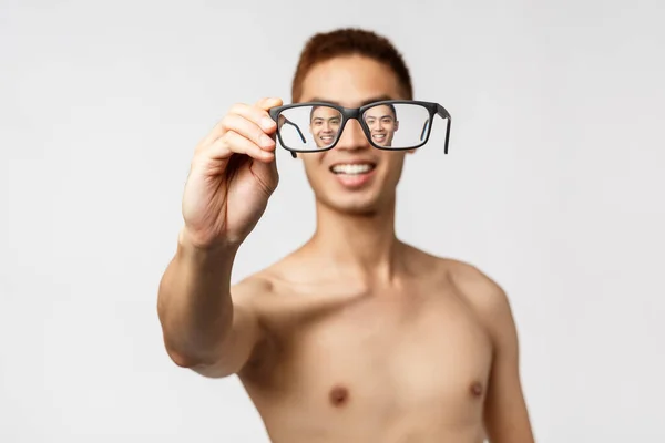 Belleza, gente y estilo de vida. Primer plano retrato de hombre asiático entusiasta con el torso desnudo, mostrando gafas, mirando a través de las gafas y sonriendo optimista, de pie fondo blanco — Foto de Stock