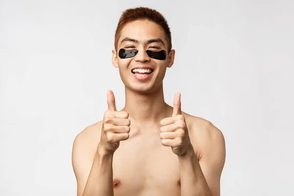 Beleza, pessoas e conceito de estilo de vida. Bonito homem asiático com tronco nu, olhando satisfeito, auto-distanciamento durante a quarentena codi19 e cuidar da pele, aplicar colírios, fundo branco — Fotografia de Stock