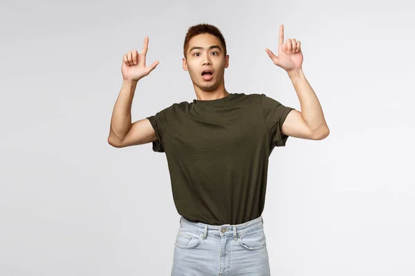 Portrait of shocked and nervous asian man look at camera surprised, pointing fingers up, showing something strange and concerning, asking question about item, grey background — Stock Photo, Image