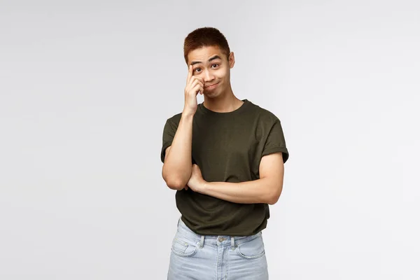 Portrait of bothered and annoyed asian guy hear nonsense, smirk and stare with disbelief, scratching forehead and look camera ignorant, standing grey background distressed and tensed — Stock Photo, Image