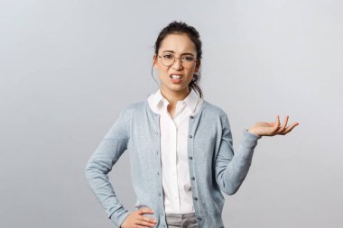 Ne olmuş yani? Kuşkucu, kibirli Asyalı kadın, korku ve muhakeme kamerası ile bakıyor, yan el kaldırıyor ve rahatsız edilmeden omuz silkiyor, korkunç ve kötü, gri bir arka plan hayal kırıklığına uğramış görünüyor