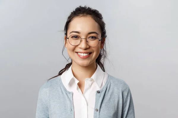 Close-up portret van aantrekkelijke, vriendelijk ogende Aziatische kantoormedewerker, werknemer of leraar in bril, brede glimlach camera met enthousiaste houding, grijze achtergrond — Stockfoto