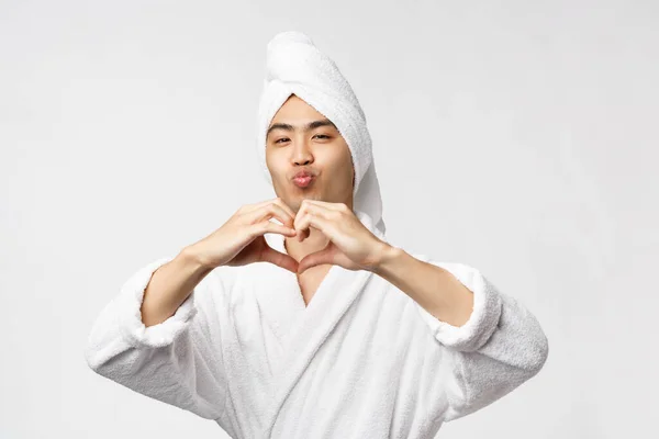Szépség, spa és szabadidő koncepció. Buta és vicces aranyos aranyos ázsiai férfi kád törölköző a fej és a fürdőköpeny, duzzogás és csókolózás arc, show szív jel, kifejezni a szeretet és együttérzés, fehér háttér — Stock Fotó