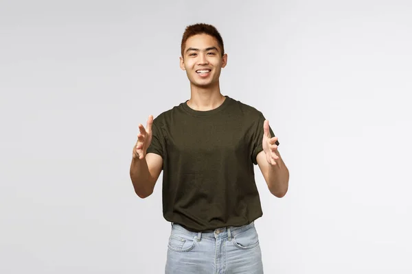Portret wesołego, szczęśliwego, zdrowego Azjaty, młodego faceta otrzymującego paczkę z dostawy online podczas kwarantanny domowej19, sięgającego po produkty, szare tło — Zdjęcie stockowe