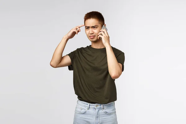 Teknologi, gaya hidup online dan konsep komunikasi. Portrait of frustrasi dan bingung, judgemental asian guy think speaker is stupid or crazy, talking on phone and cringe dishappy — Stok Foto