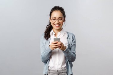 Ofis hayatı, iş hayatı ve insan konsepti. Mutlu Koreli kadın mesaj atıyor, cep telefonu kullanıyor, akıllı telefon ekranına gülümsüyor, komik bir konuşma yapıyor, internetten video izliyor.