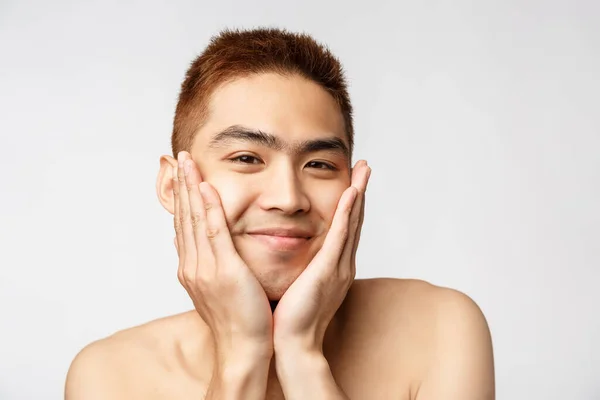 Belleza, cuidado de la piel y los hombres concepto de salud. Retrato de chico desnudo asiática tonta, adorable, tratando sus imperfecciones, sentirse hermosa y feliz, tocando la cara y sonriendo ampliamente, fondo blanco — Foto de Stock