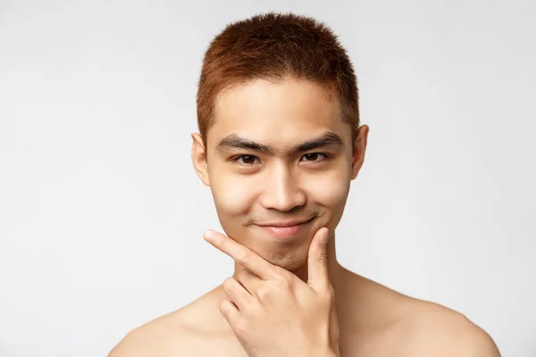 Krása, péče o pleť a zdraví mužů. Snímek hlavy inteligentní a kreativní asijské mladý muž stojící nahý trup, vypadat potěšeně, dotek brady a usmívající se fotoaparát, mají nápad, vymyslet-up plán — Stock fotografie