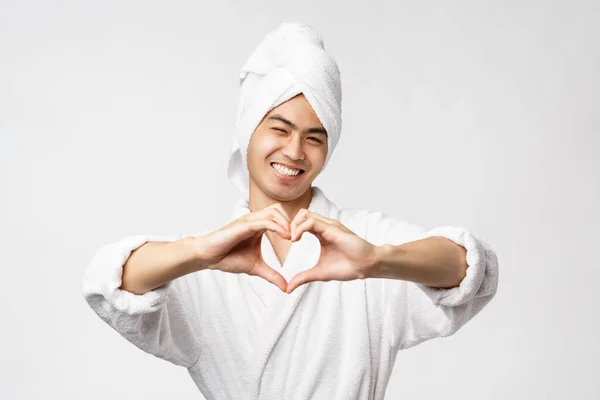 Szépség, spa és szabadidő koncepció. Portré jóképű romantikus ázsiai férfi fürdőköpeny és törülköző, mosolygós boldog, mutatják szív jel a mellkas, kifejezni együttérzés és a szeretet, fehér háttér — Stock Fotó
