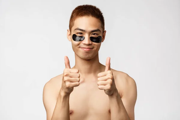 Belleza, gente y estilo de vida. Retrato de satisfecho, despreocupado guapo asiático hombre con el torso desnudo, mirando complacido, sonriente show thumb-up recomiendo parcheado para lucir en forma y saludable — Foto de Stock