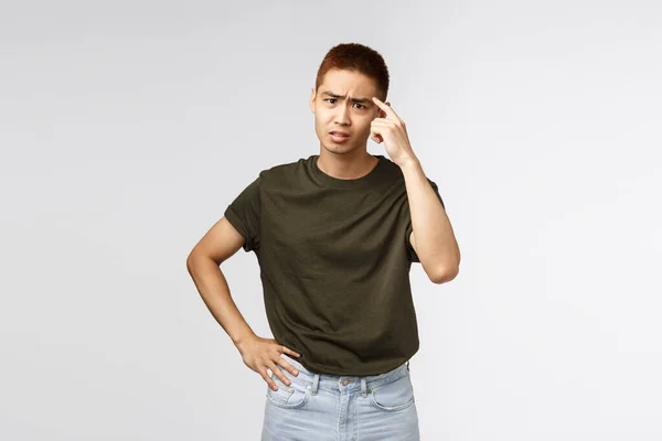 Portrait of annoyed and pissed-off asian man scolding person for being stupid and acting irrational, tap on temple accusing friend being crazy, complaining and frowning displeased, grey background — Stockfoto