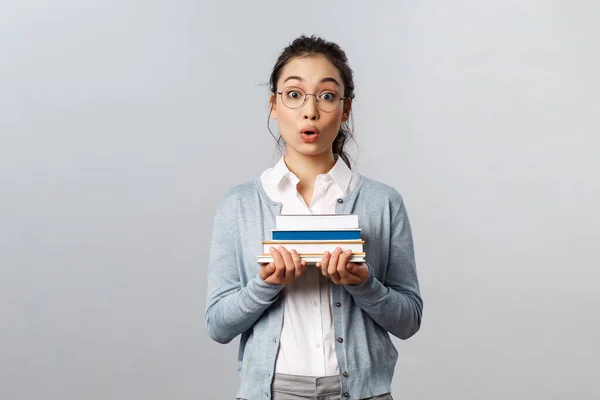 Éducation, enseignants, université et écoles concept. Surpris et amusé intelligent nerdy asiatique femme étudiante, transporter des livres pour les cours, regarder caméra émerveillée et impressionnée, écouter histoire intéressante — Photo